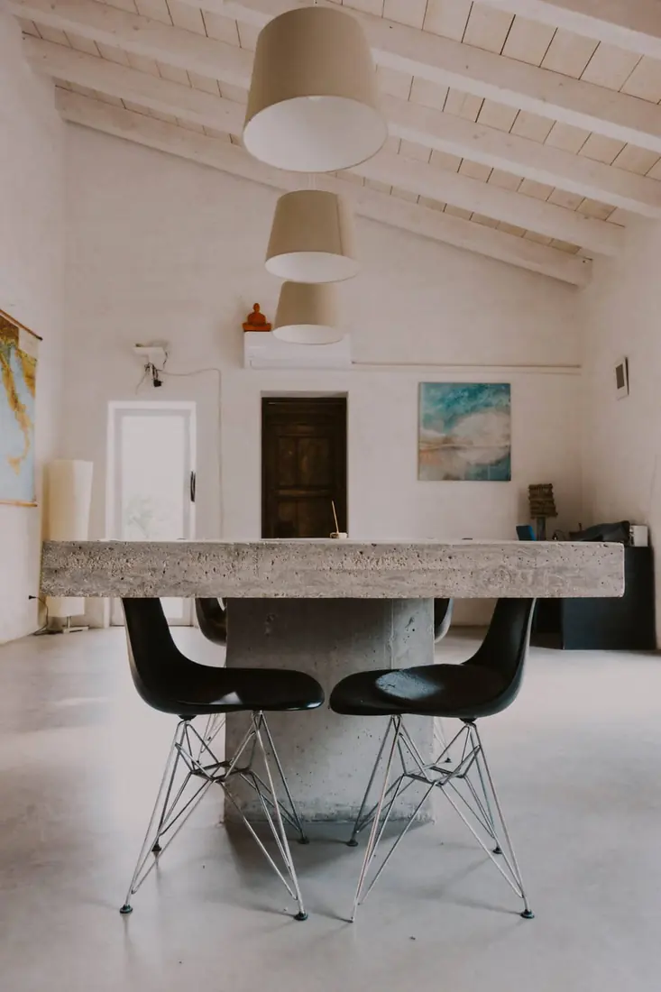 The long concrete dining table with black chairs under three paper pendant lamps