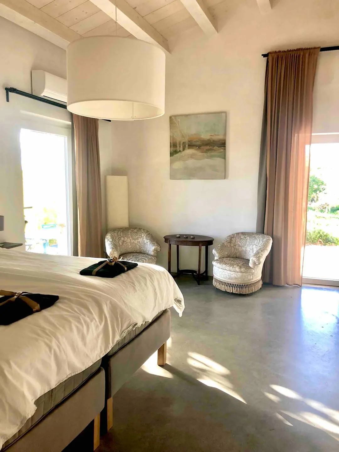 Room 1: a bright bedroom with a king-size bed, two armchairs, a pendant lamp and a window onto the fields