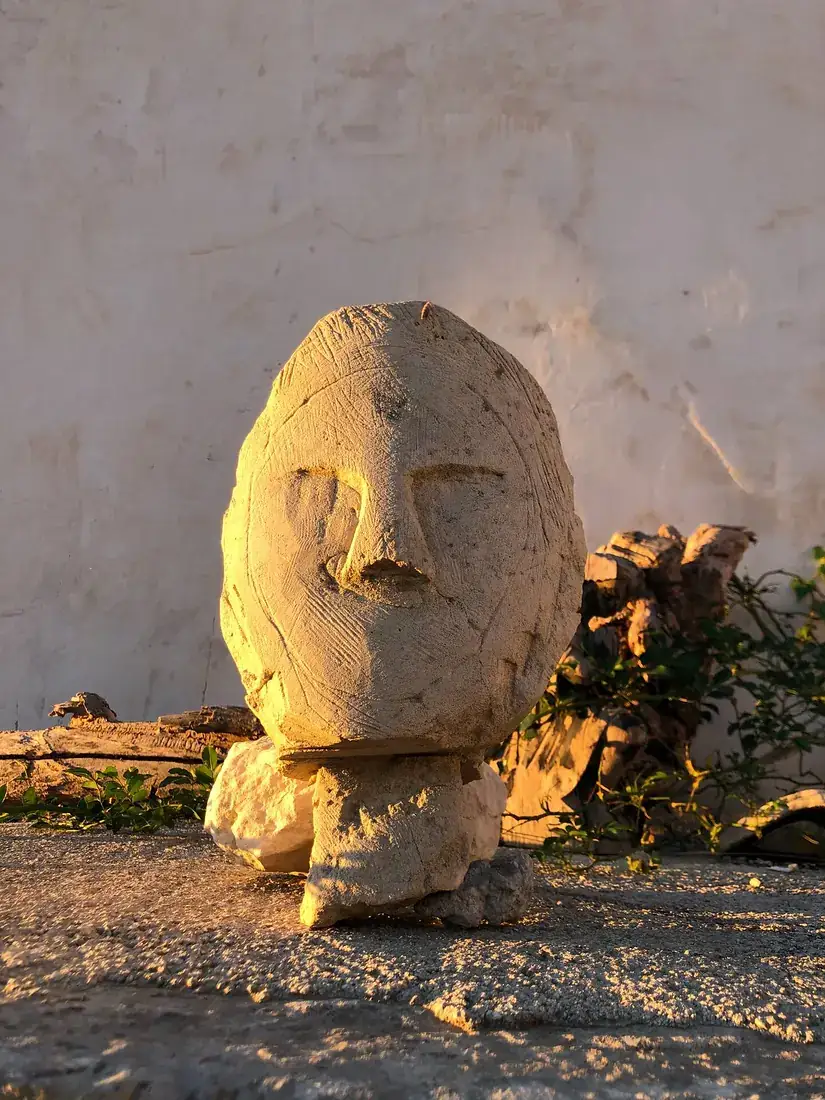 A carved stone head standing among the old stones, warm in the evening light